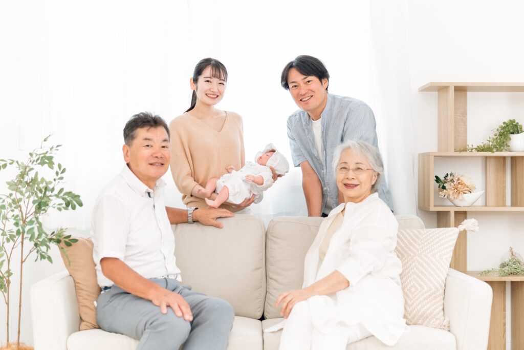 赤ちゃんを抱いた両親と祖父母が笑顔で並ぶ3世代の集合写真